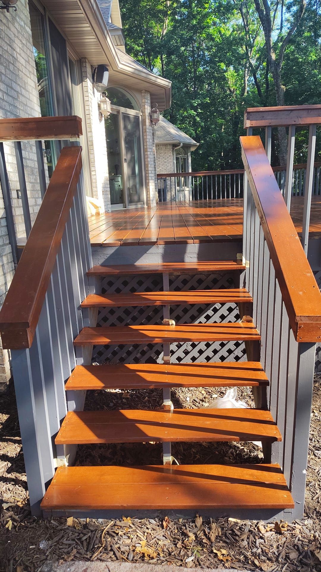 Wooden deck stairs with stained treads and painted railing. Sunlight shines on the deck.