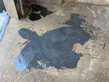 Dark liquid spill on a concrete floor near a wooden structure.