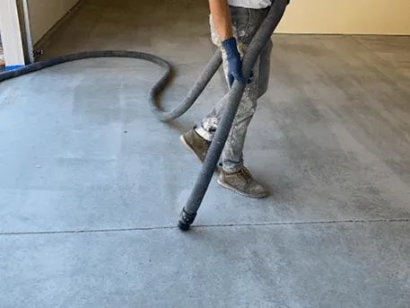 Person in work clothes vacuuming a concrete floor with a large hose.