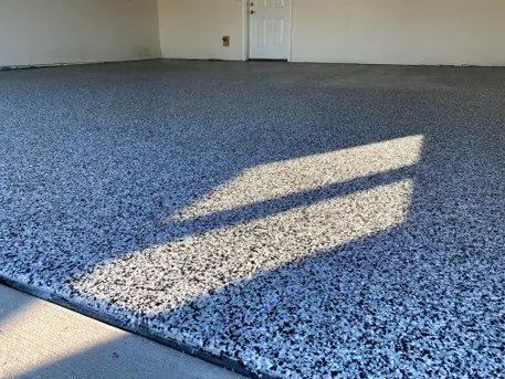 Gray speckled epoxy garage floor. Sunlight casts shadows from the garage door.