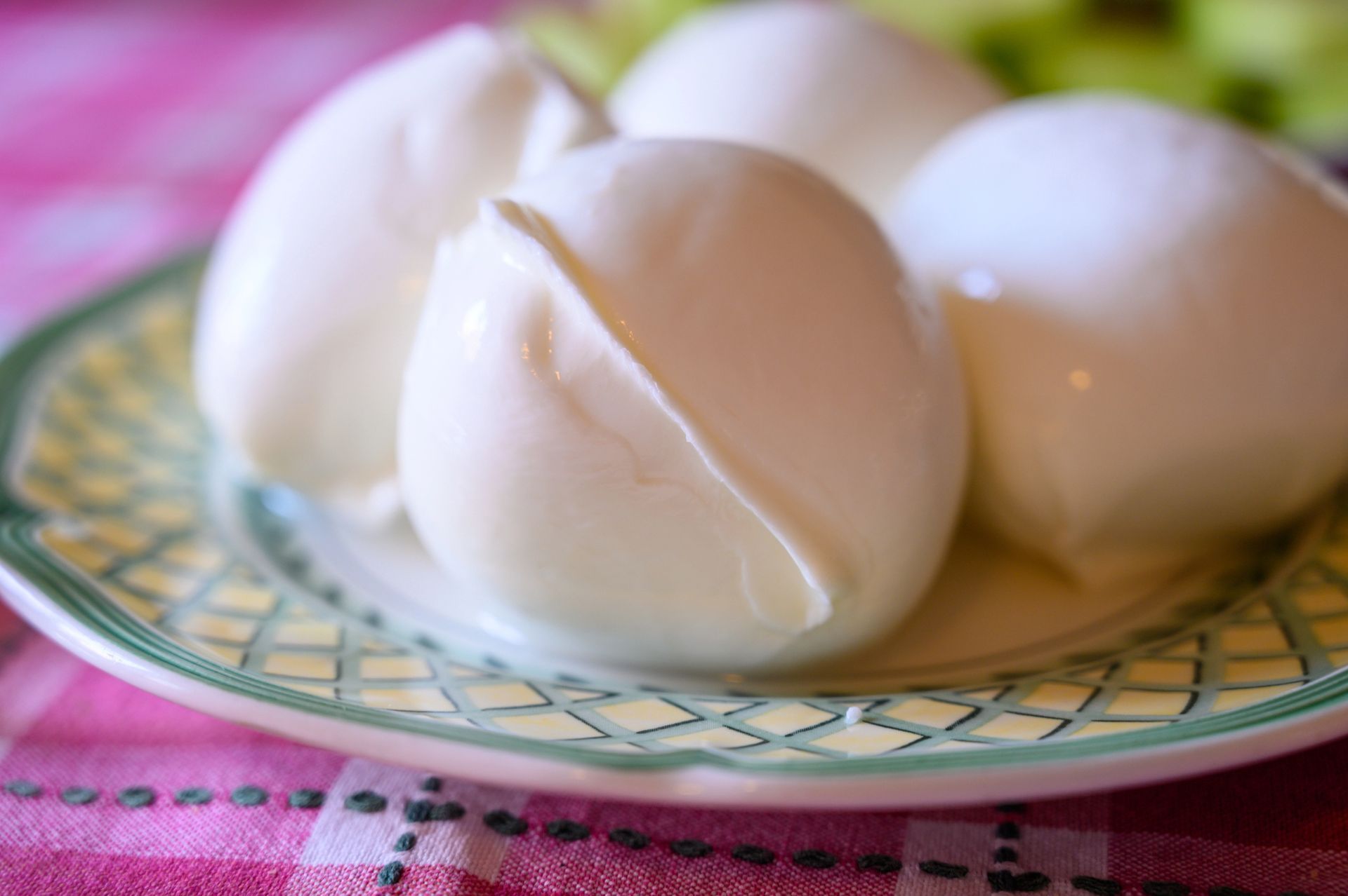 Mozzarella bianca su un piatto decorato, tovaglia a quadretti rosa sullo sfondo.