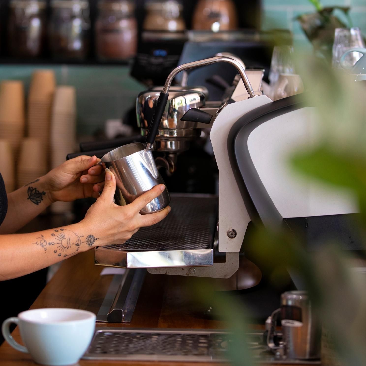 A Woman Is Pouring Milk Into A Coffee Machine — The Real Grocer In Golden Beach, QLD