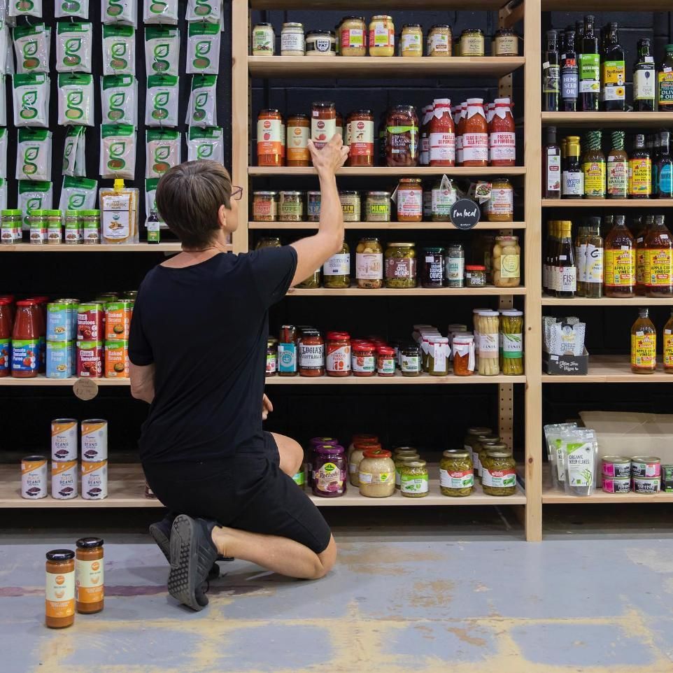 A Man Is Kneeling Down In Front Of A Shelf Full Of Food Items — The Real Grocer In Golden Beach, QLD