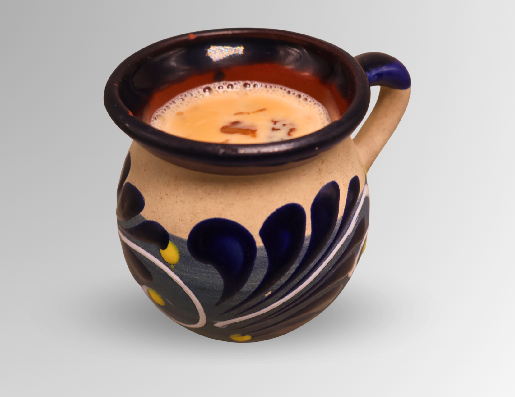 Clay mug with blue floral design filled with a light brown beverage.