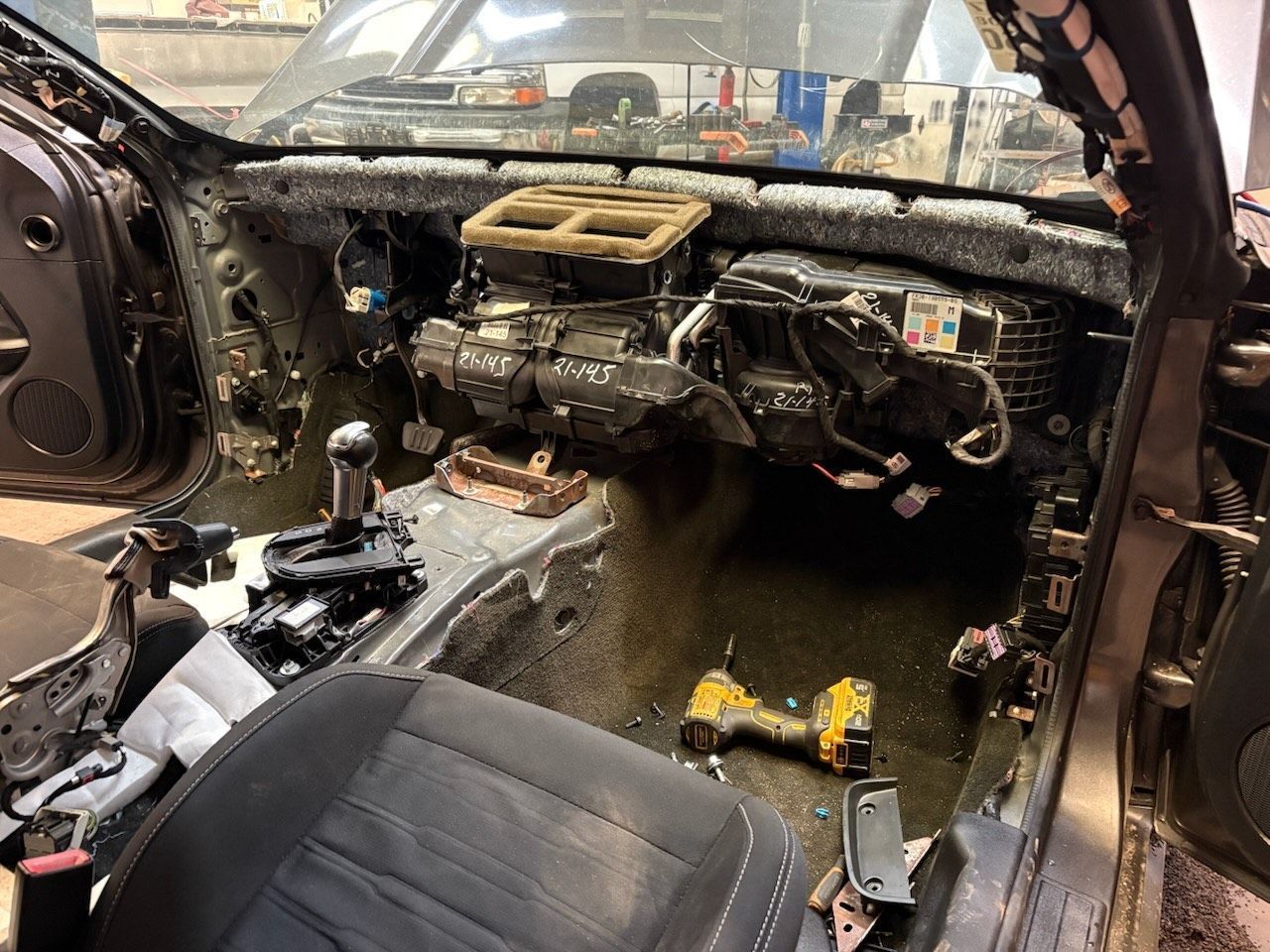 Interior of a car undergoing disassembly. Dashboard and components are removed, exposing wires, insulation, and the car's frame.