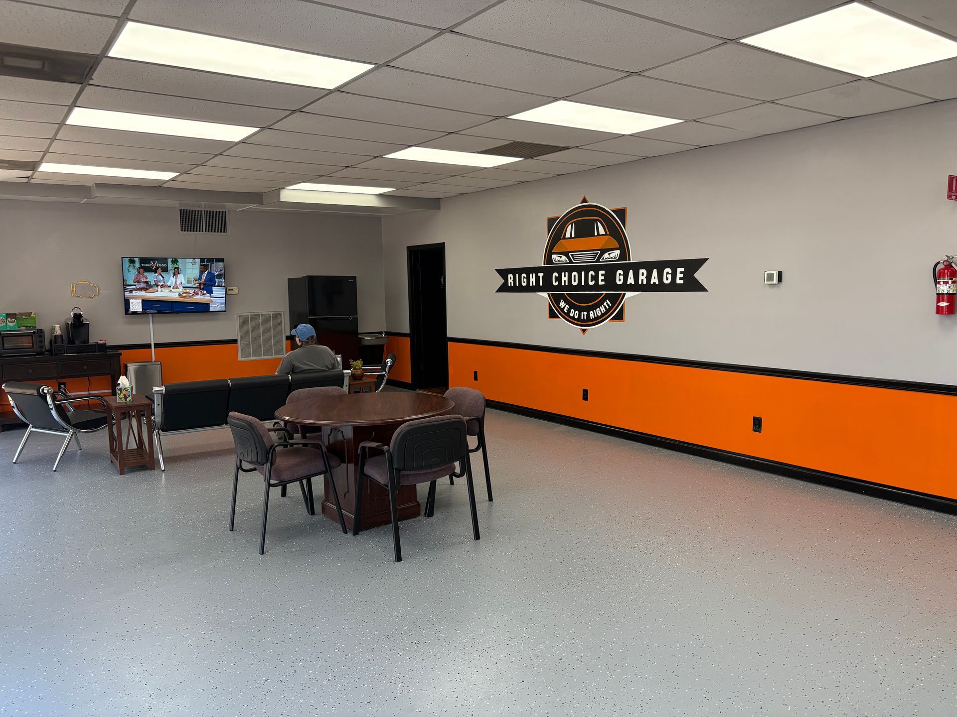 Waiting area with orange and gray accents, tv, chairs, and logo.