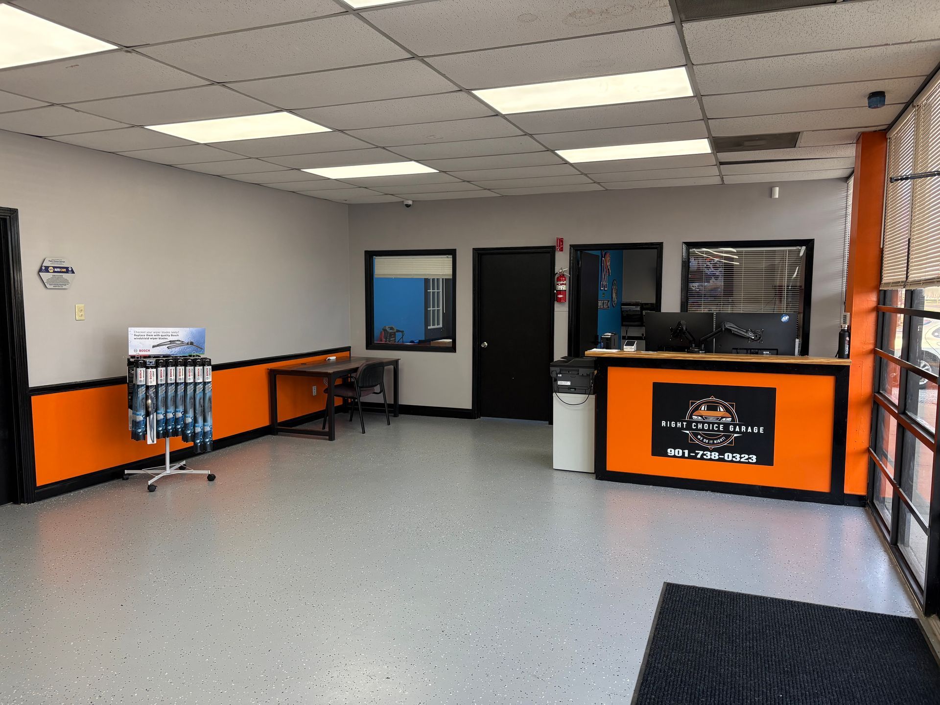 Interior of an auto shop's waiting area with an orange and black front desk, gray floor, and a display rack.