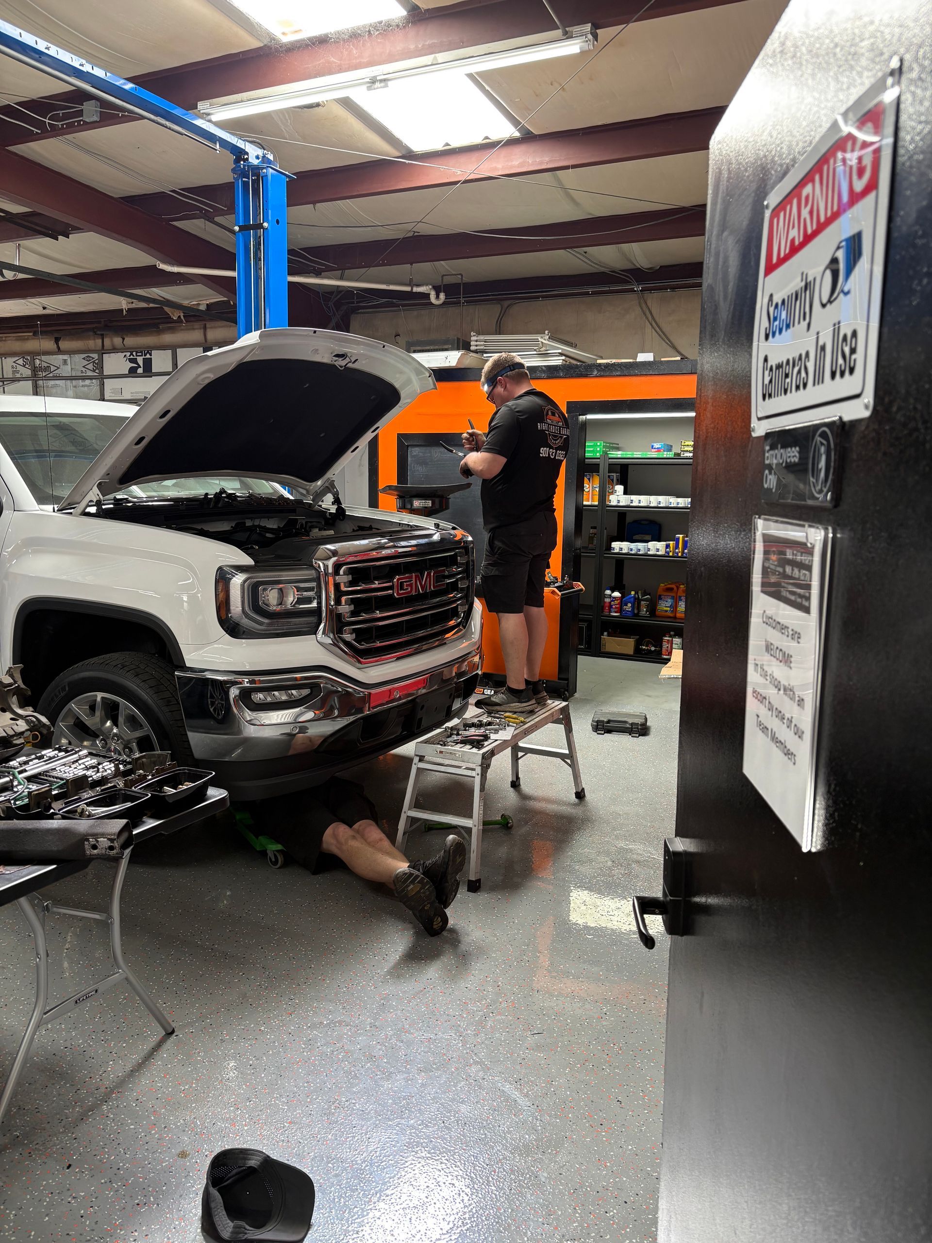 Mechanics working on a white truck in a garage. One under the truck, one standing near a work station.