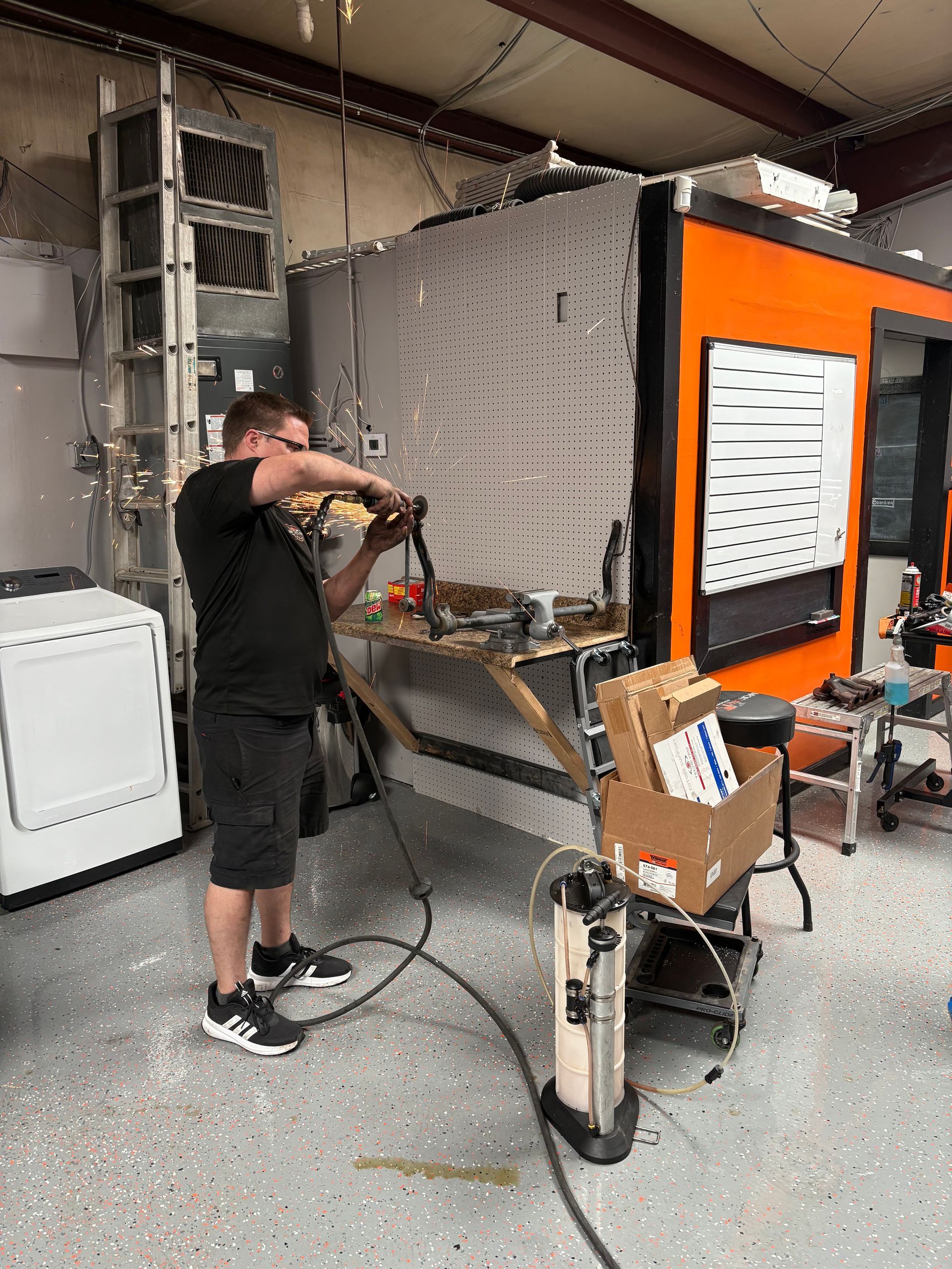 Man working with tools in a workshop, near a large orange and gray structure.