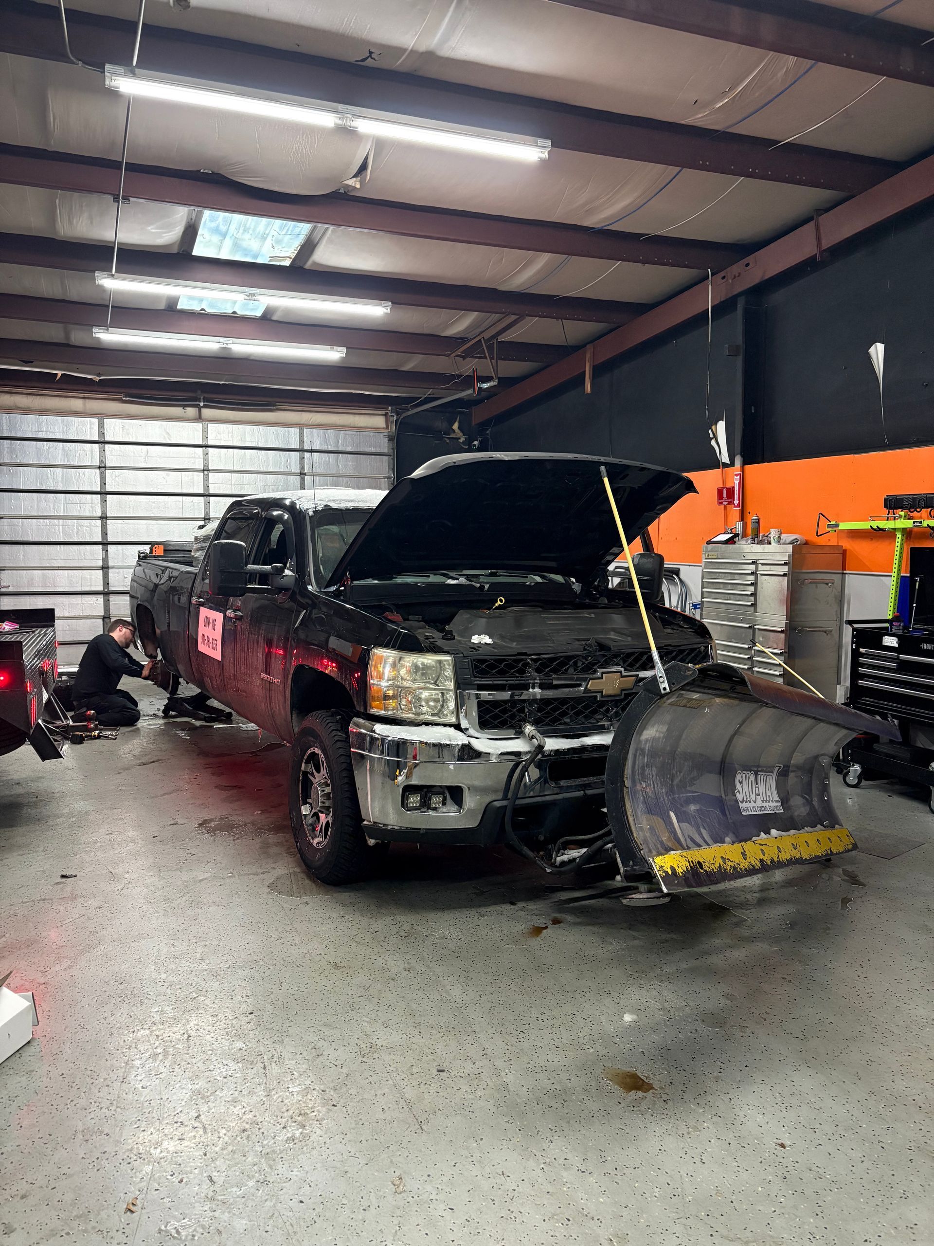 The image depicts two individuals working on a black Mercedes-Benz vehicle, likely performing window tinting or a similar detailing service.