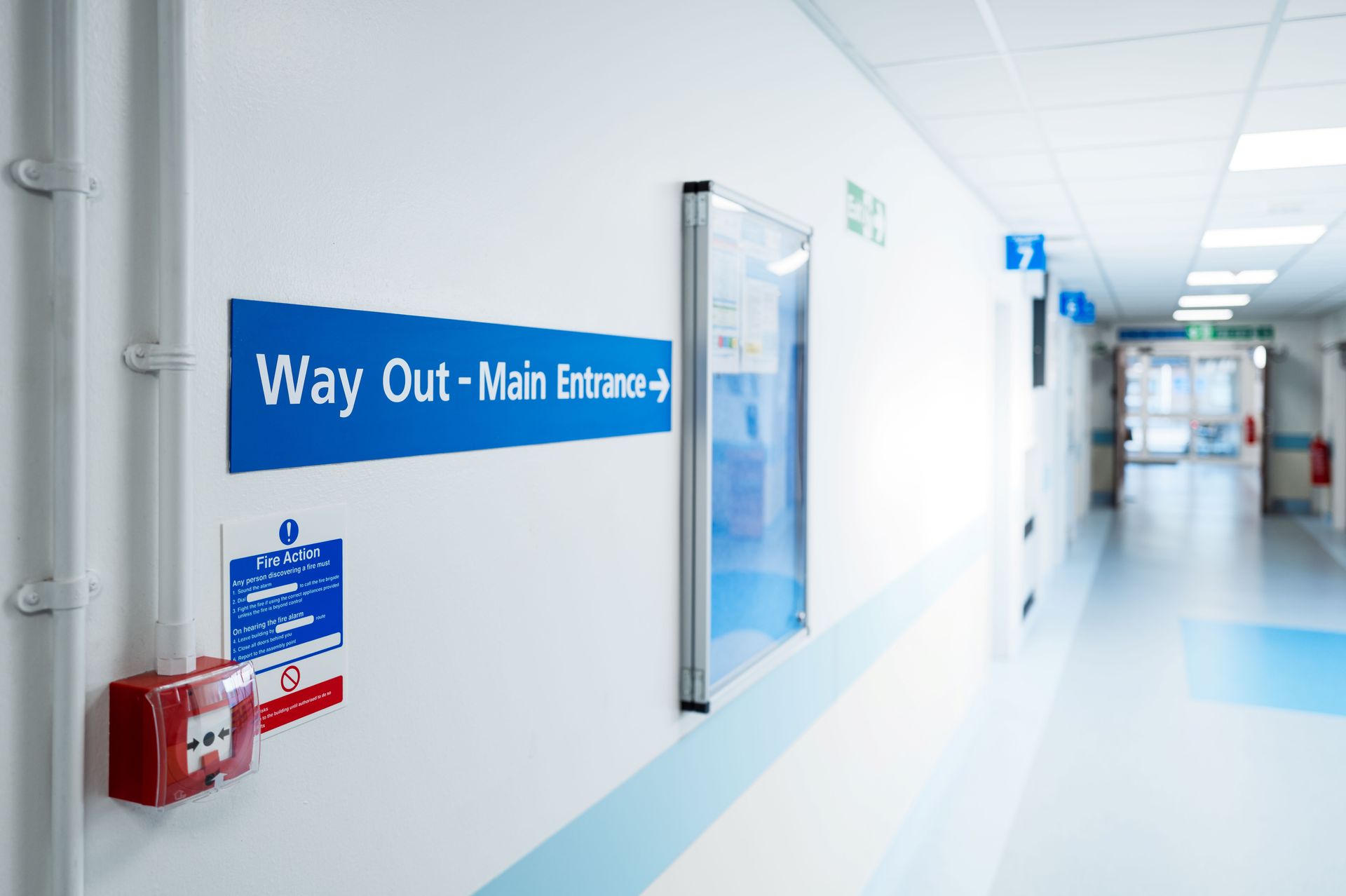 Hospital corridor with clear “Way Out – Main Entrance” signage on a clean hallway with lighting.