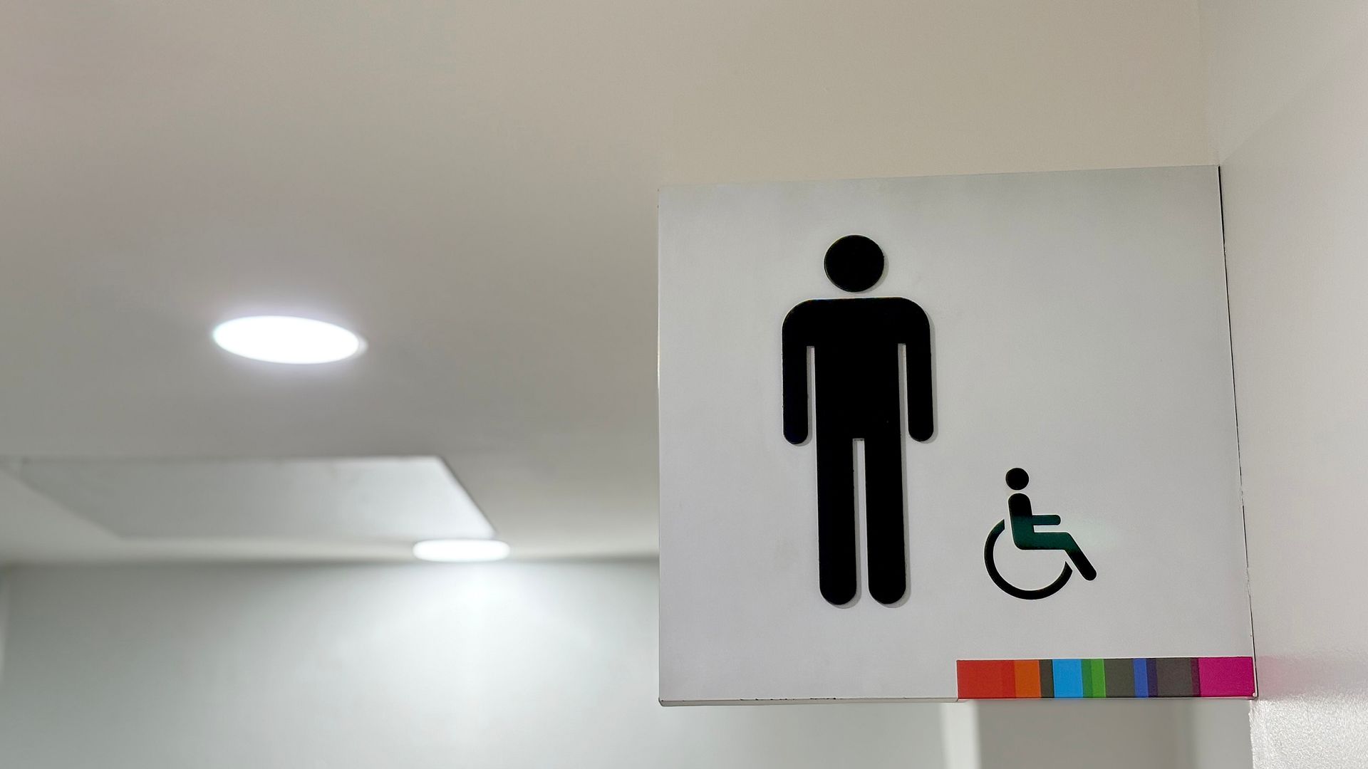 Restroom sign displaying standard and wheelchair accessibility symbols mounted in a clean hallway.