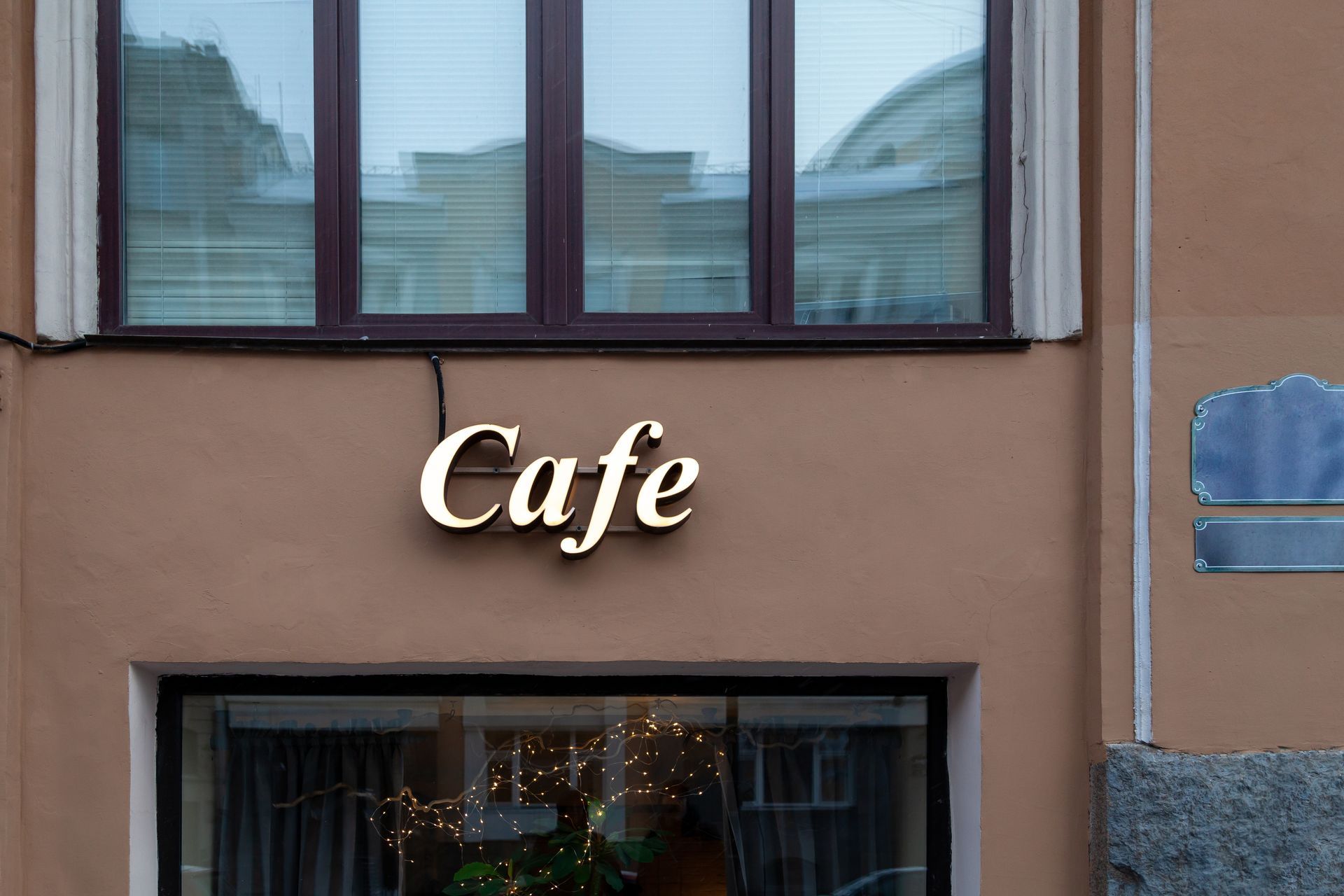 An exterior café sign is mounted above a storefront window on a city building.