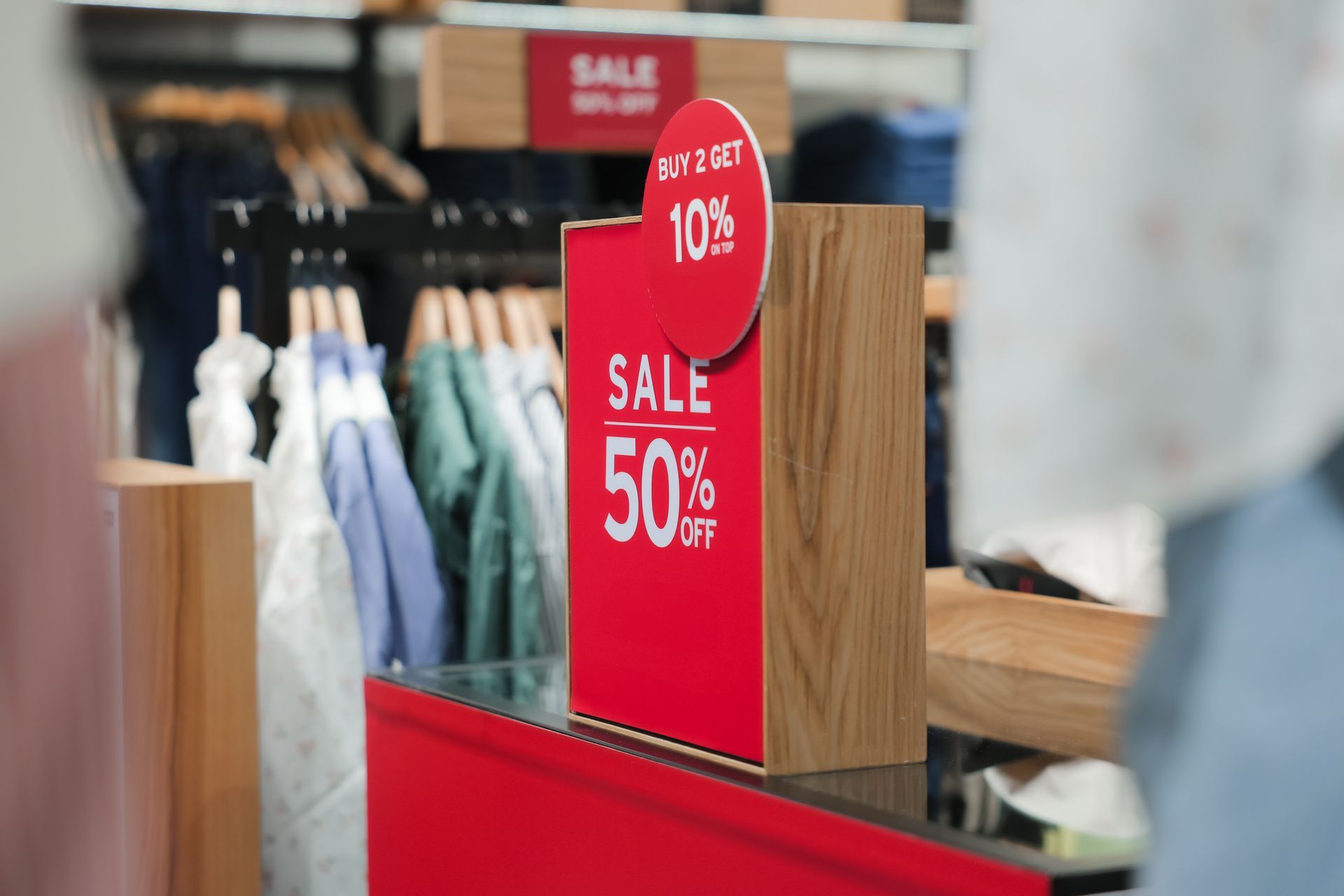 Red sale sign in a clothing store offering 50% off and extra discount for buying two items.