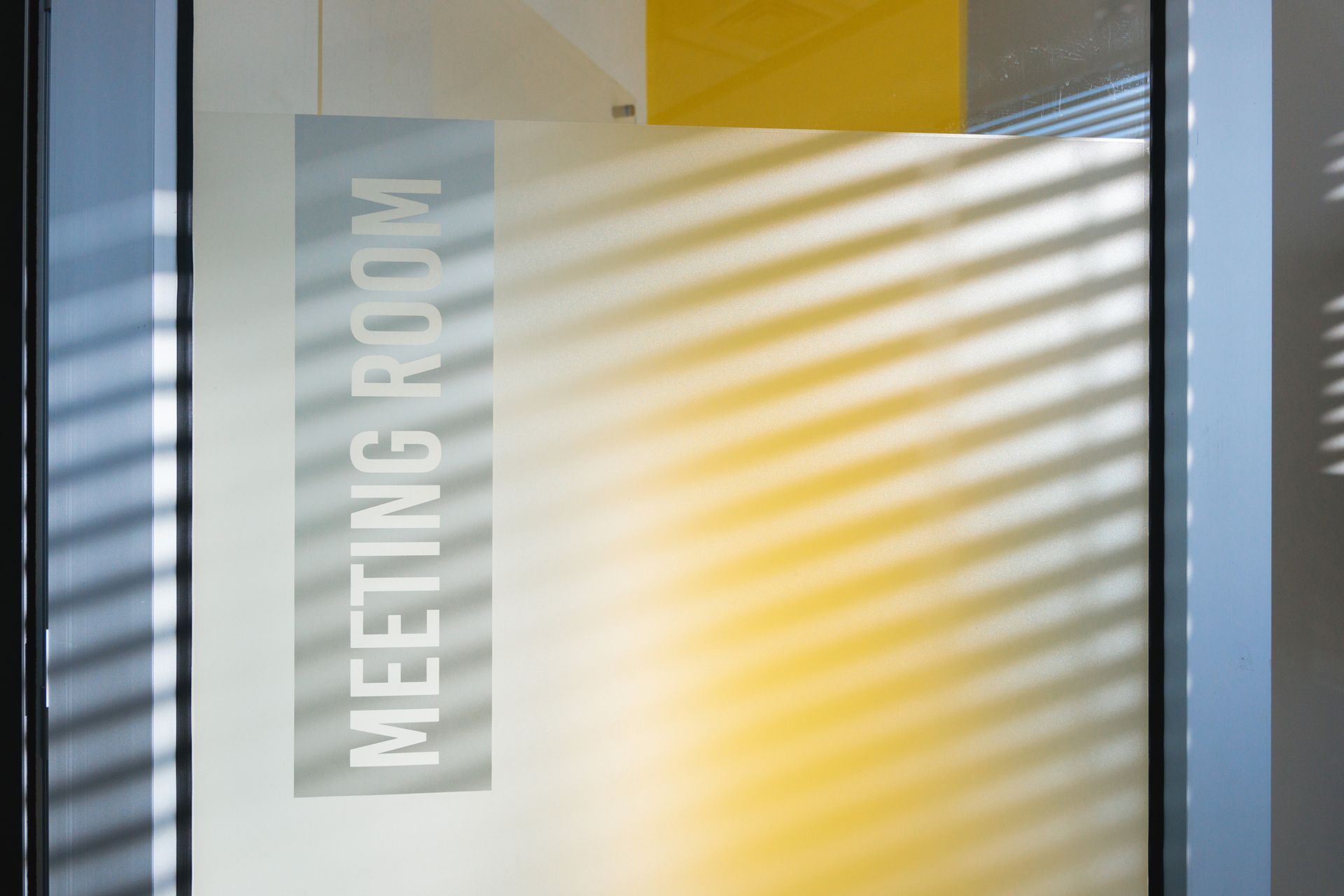 Frosted glass door labeled 'Meeting Room' with soft shadows from nearby window blinds.