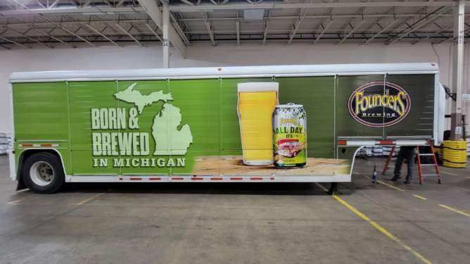 A green and white truck with a beer advertisement on it is parked in a warehouse.