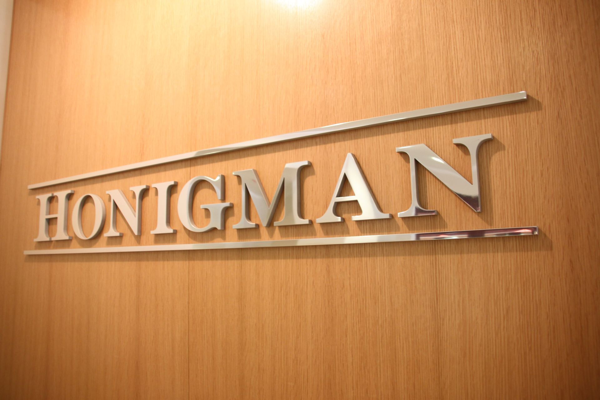 HONIGMAN sign on a wooden wall. Silver letters and horizontal bars.