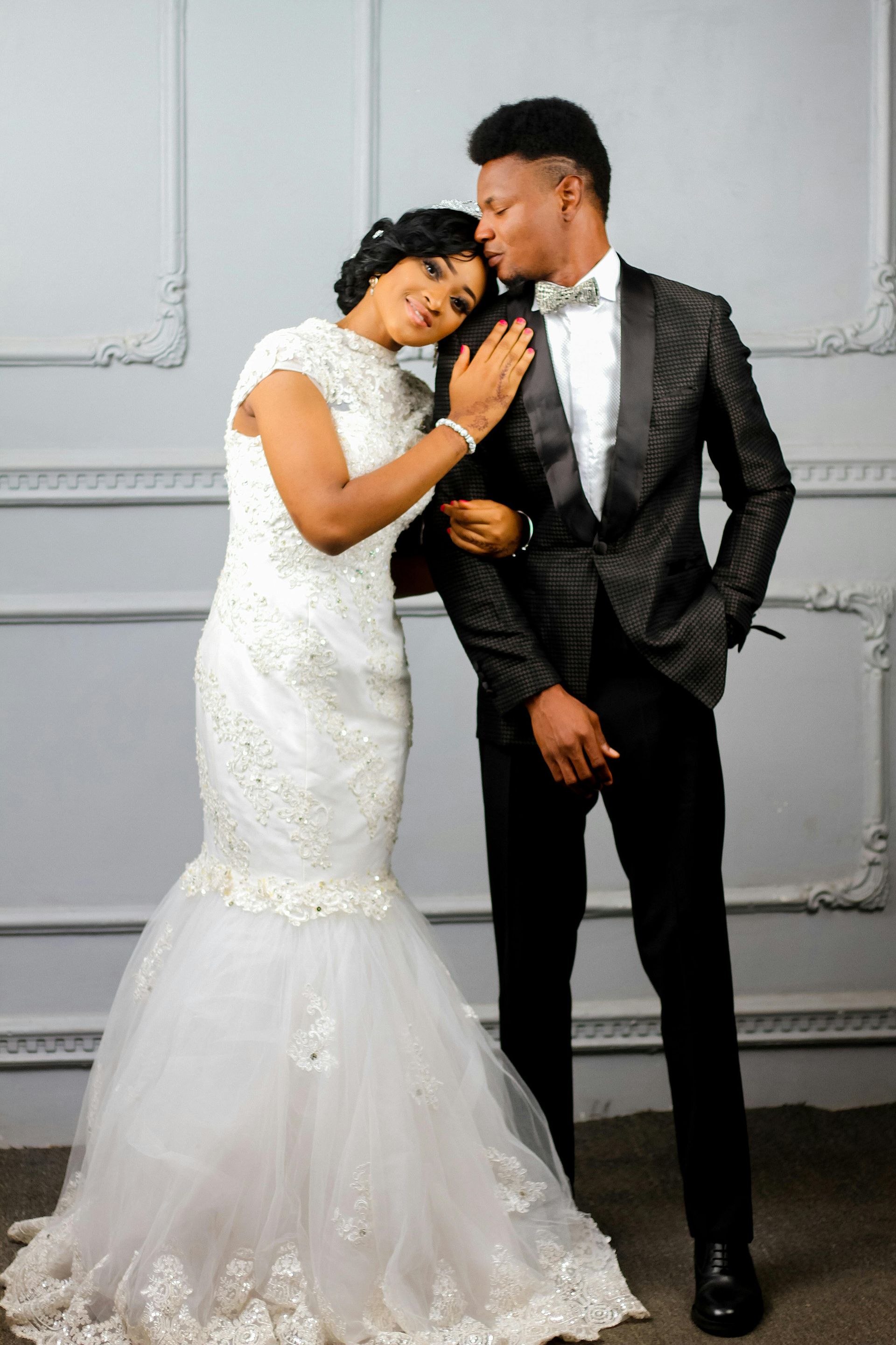 A bride and groom are posing for a picture in front of a white wall.