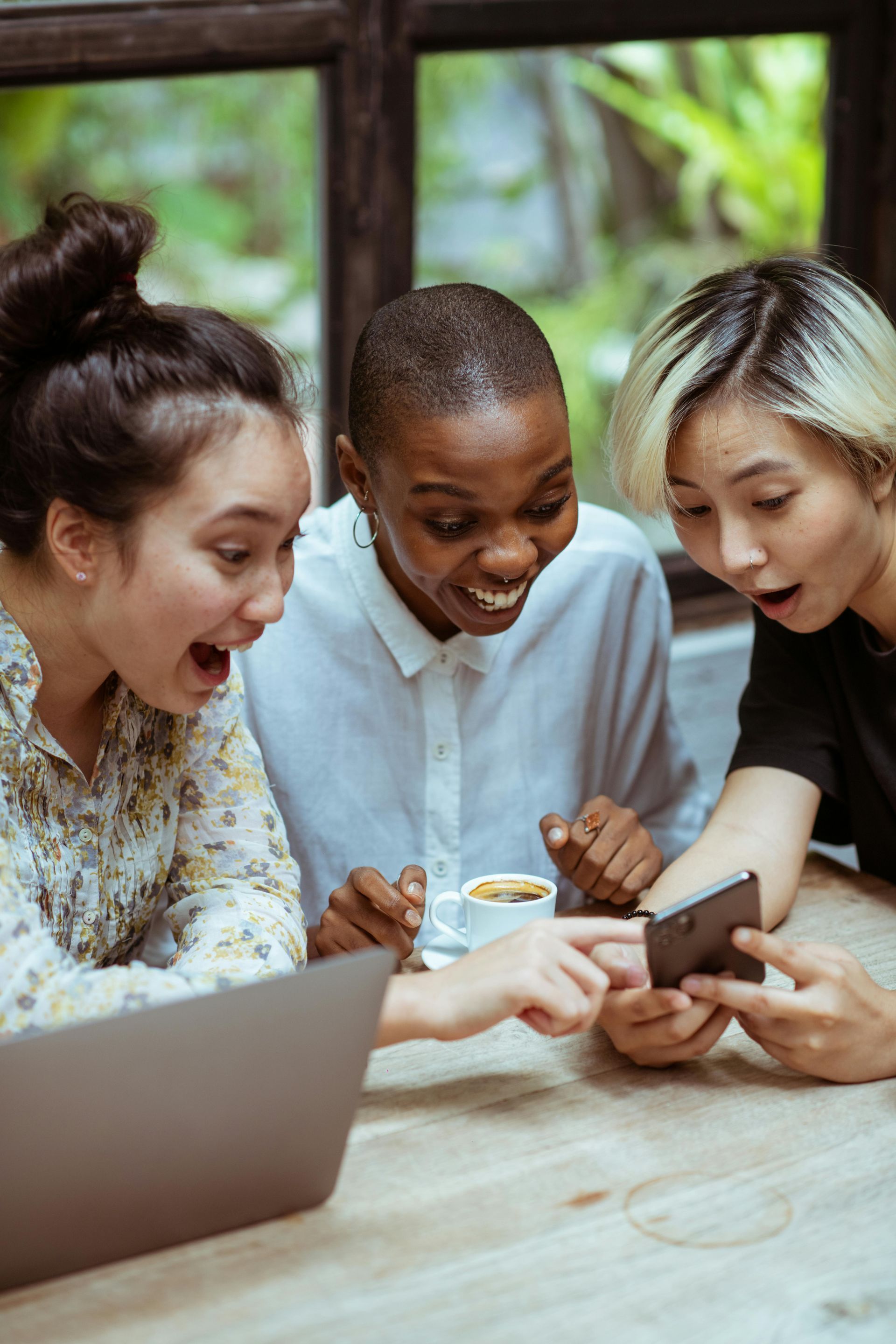 Three women are sitting at a table looking at a cell phone.