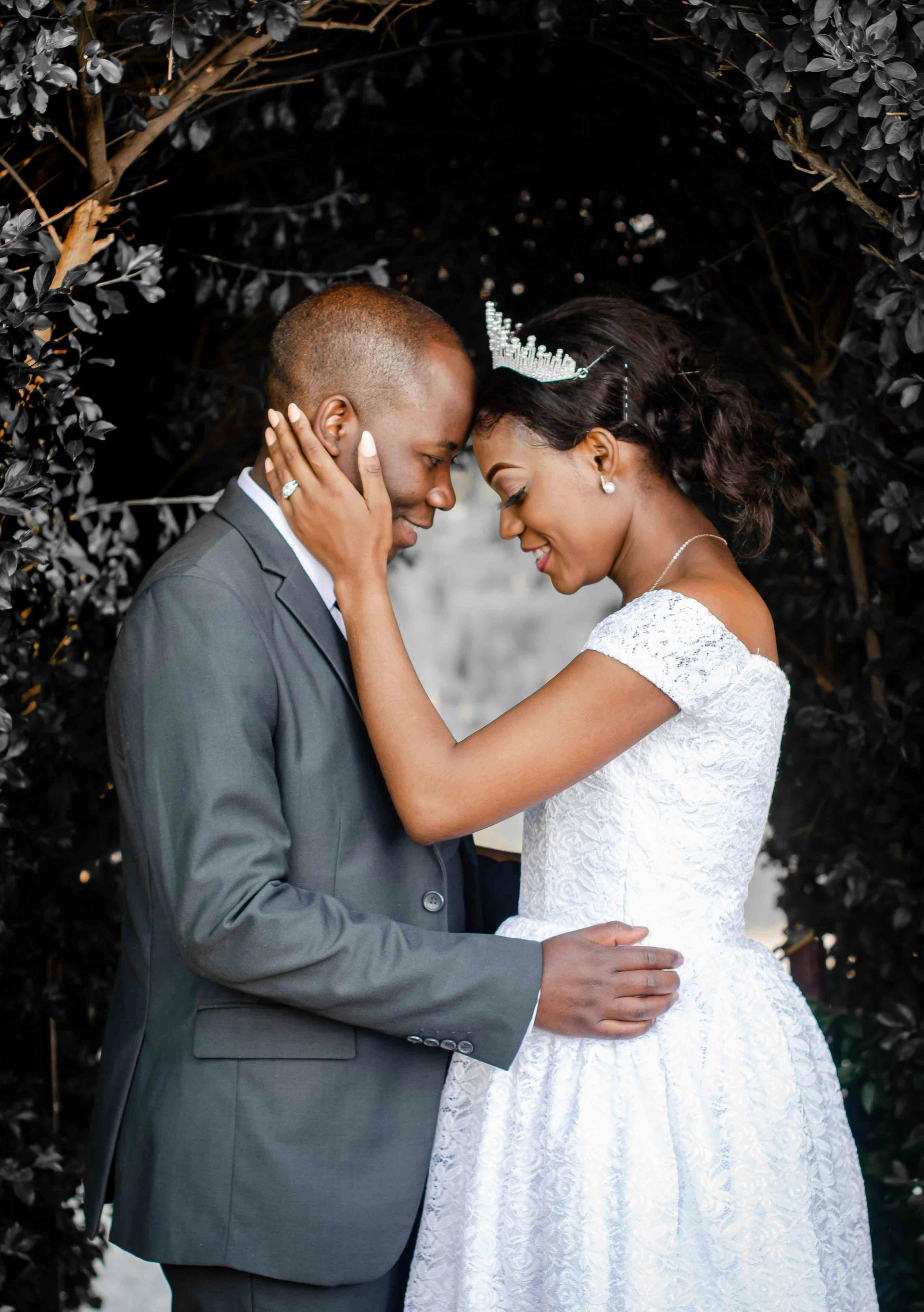 A bride and groom are standing next to each other and touching their foreheads.