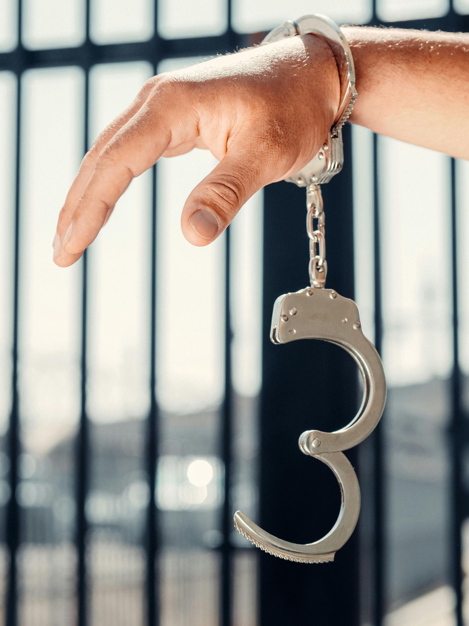 Hand in handcuffs in front of a blurred jail cell.