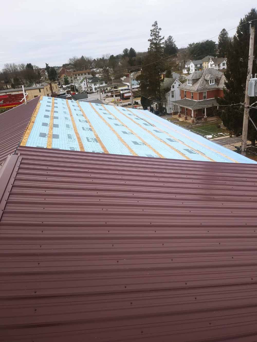 Metal roof under construction; brown installed section, blue insulation, town in background.