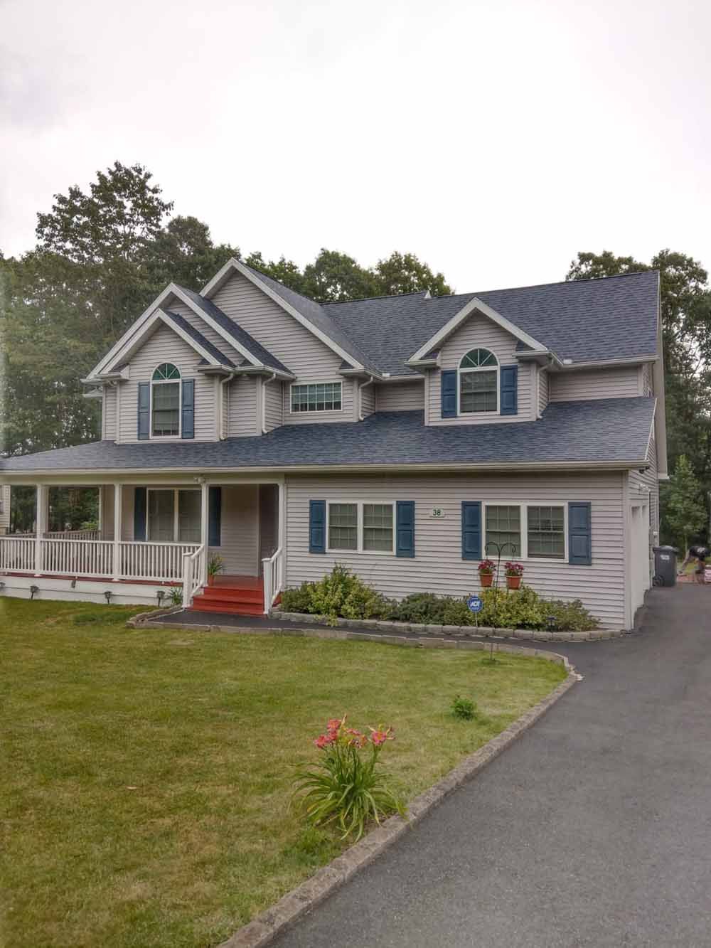 Two-story house with blue shutters, light siding, and a porch, surrounded by green grass and a driveway.