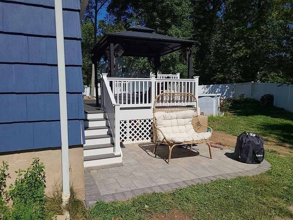 A deck with gazebo, white railing, and steps. A chair sits on the patio with a backpack.