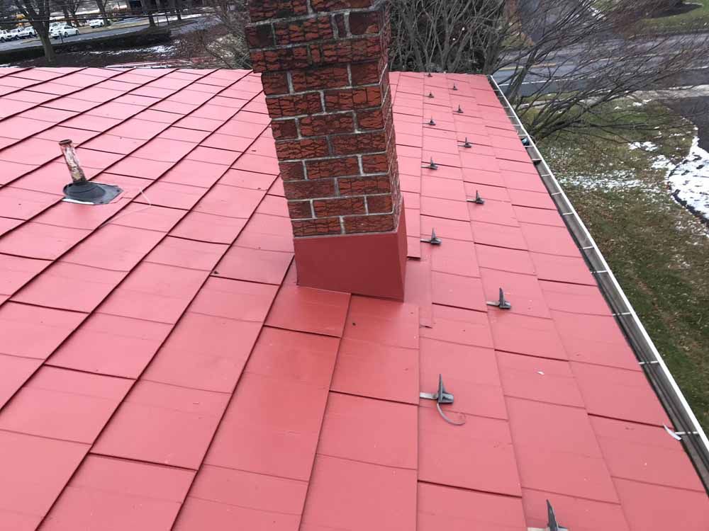 Red roof with brick chimney, snow guards, and a vent pipe.