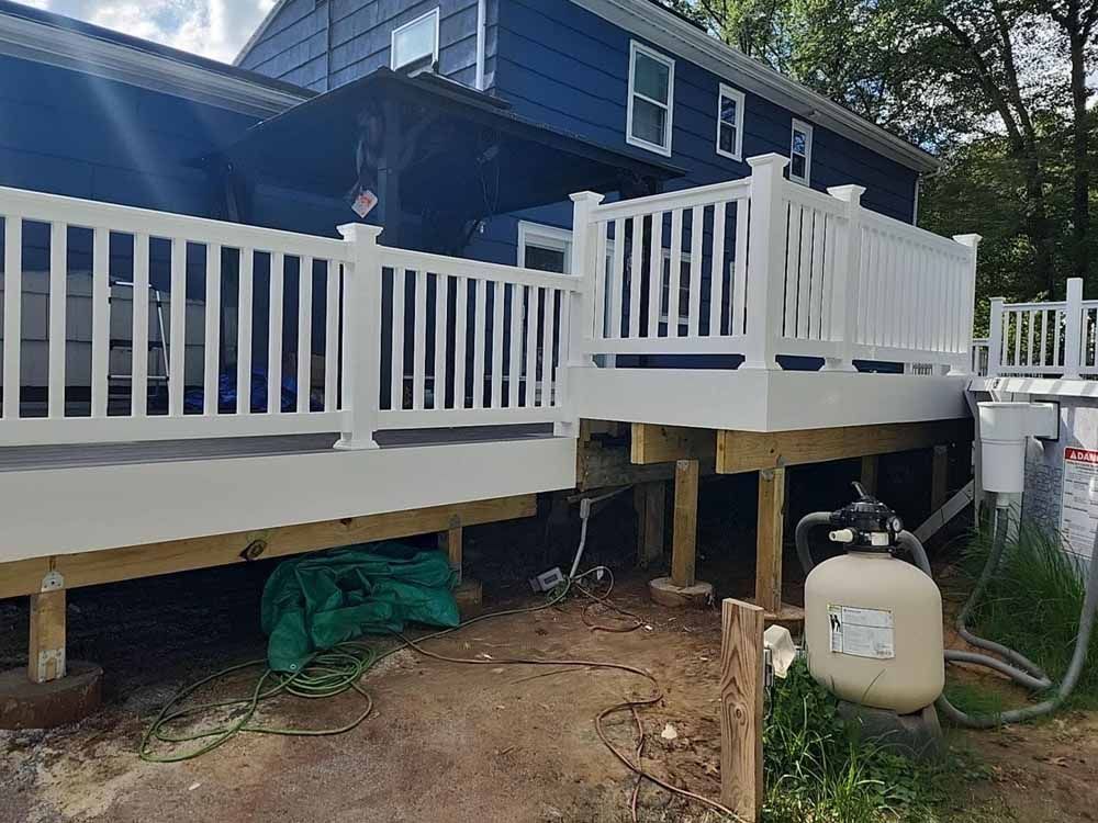White deck with railing extends from a blue house. Pool equipment is visible below the deck.