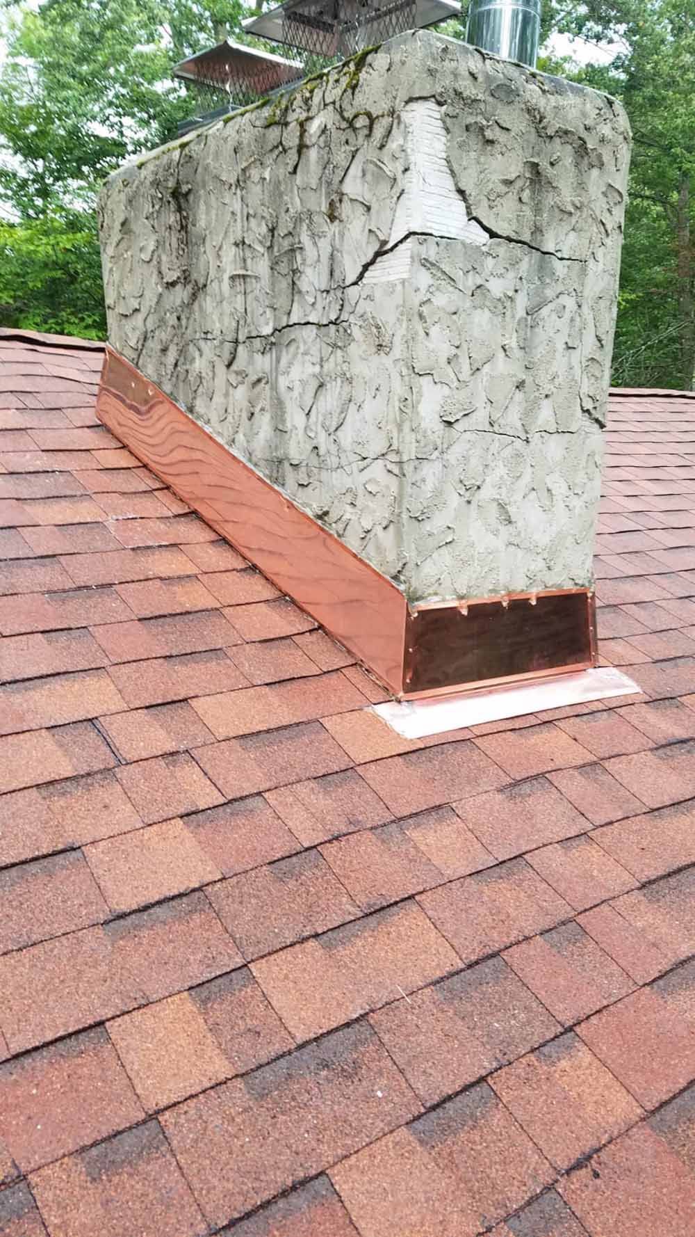 Copper flashing around a chimney on a shingle roof, showing deterioration.