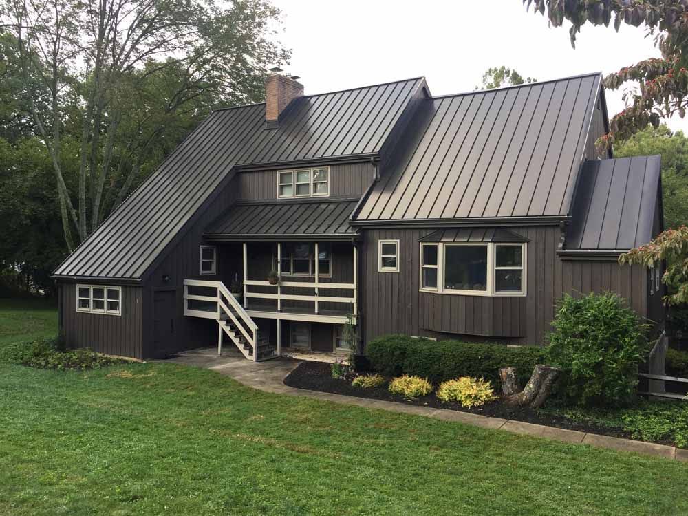 Dark brown house with a metal roof and white trim, nestled in greenery.