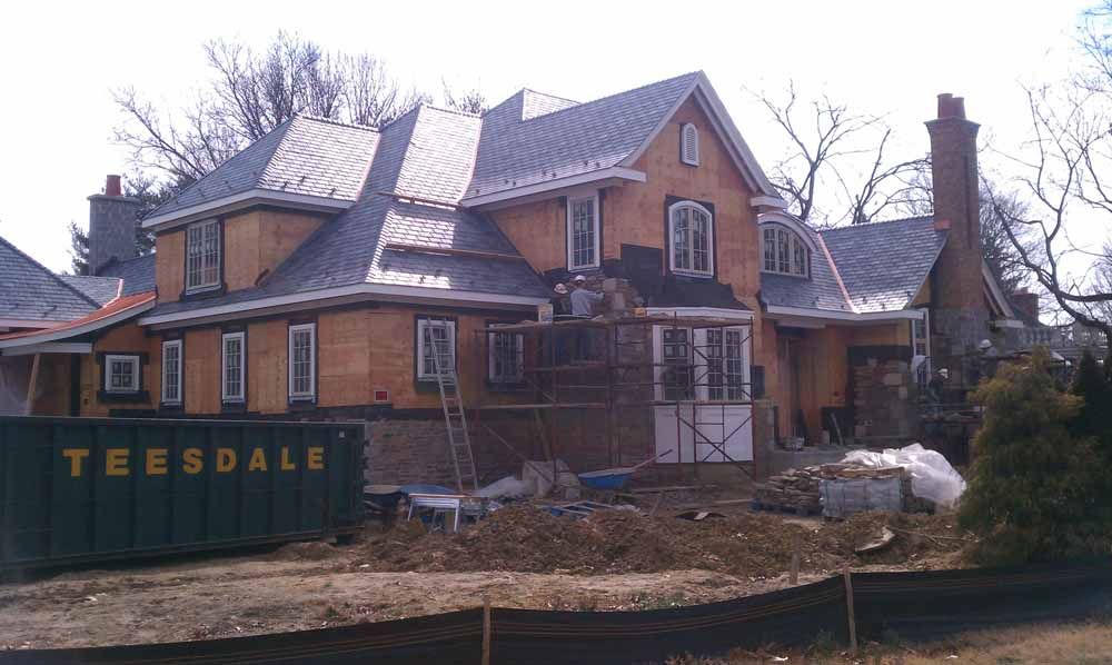House under construction with wood siding, gray roof, and a dumpster.