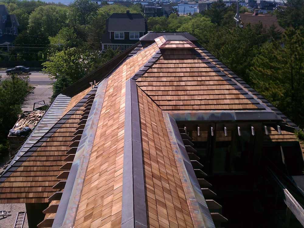Wooden shingle roof with metal flashing, viewed from above. Sunny day, trees in the background.