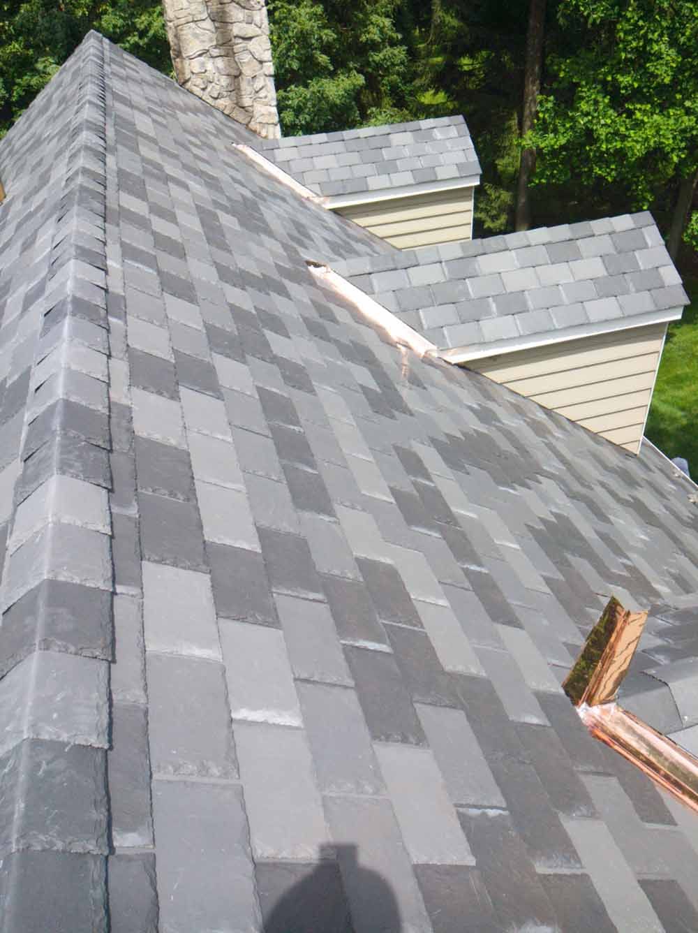 Gray shingled roof with copper flashing. Overlooking a light-colored home with other gray roofs and trees.