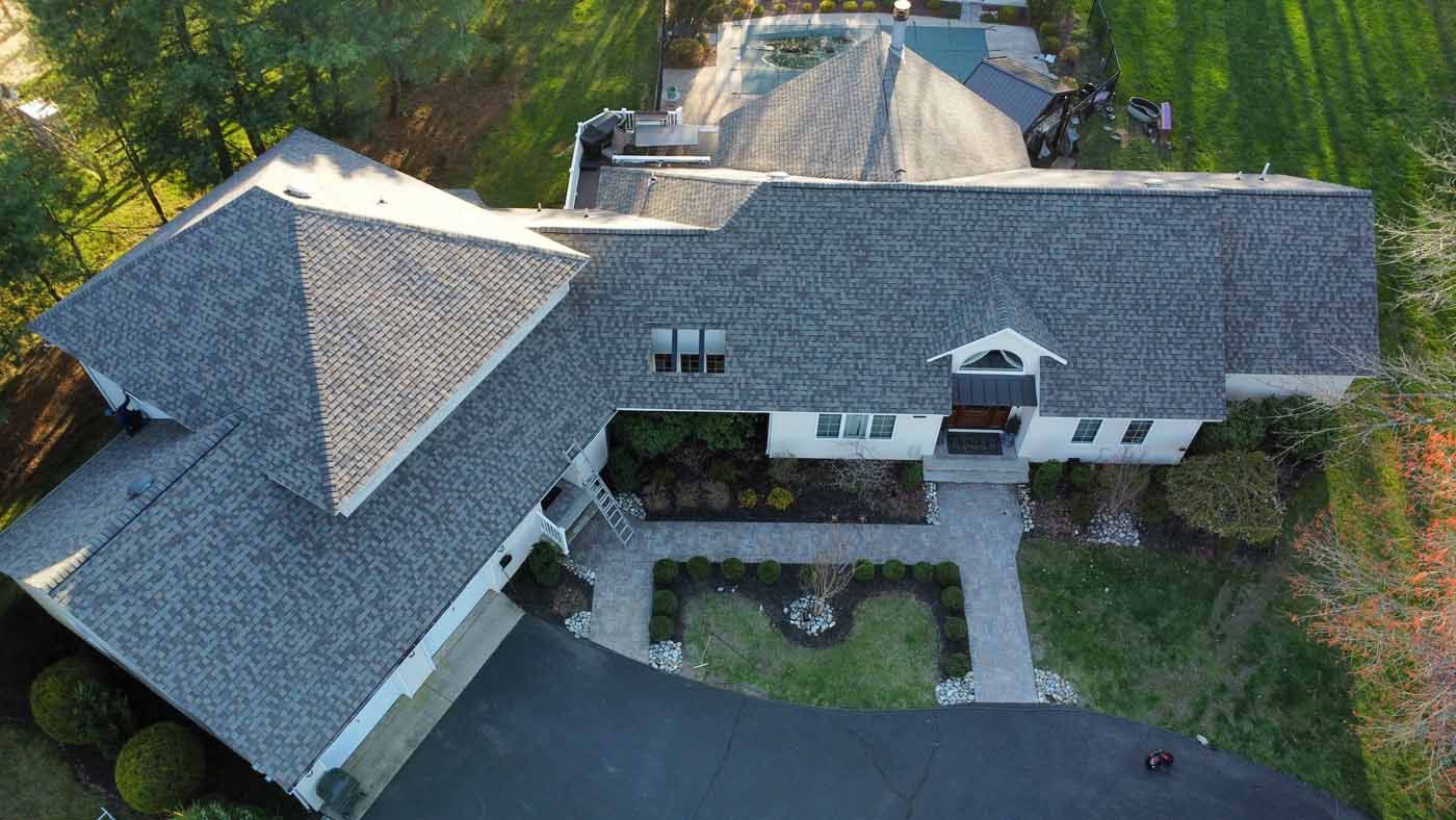 Aerial view of a house with a gray roof, black driveway, and landscaped yard.