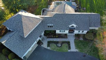 Aerial view of a house with a gray roof, black driveway, and landscaped yard.