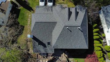 Overhead view of a house with a gray roof, two cars, and greenery in a residential area.