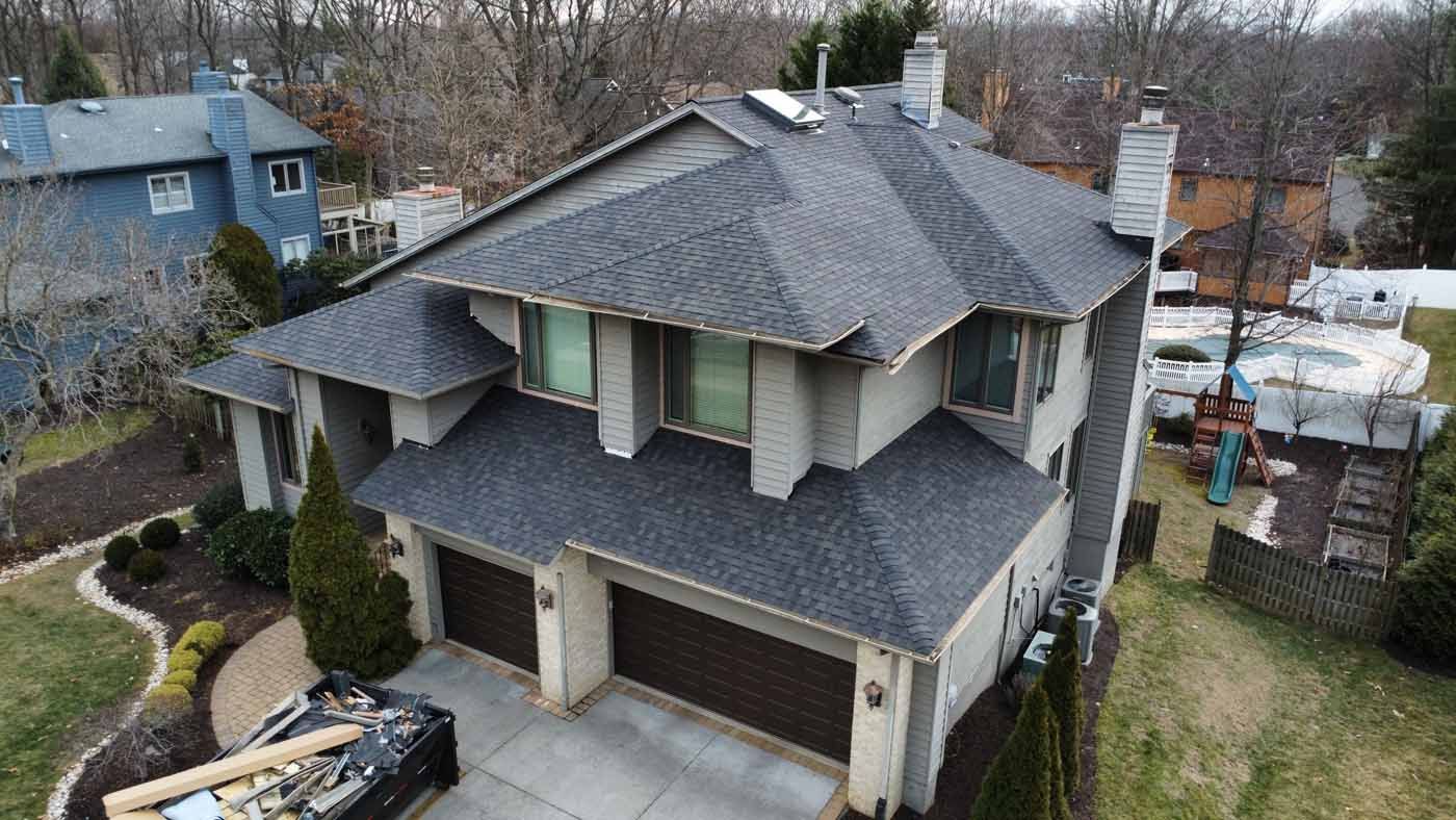 A two-story house with a new grey roof, two-car garage, and surrounding greenery in an outdoor setting.