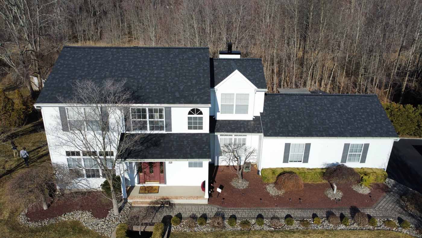 White two-story house with black roof, red door, surrounded by bare trees and landscaping.