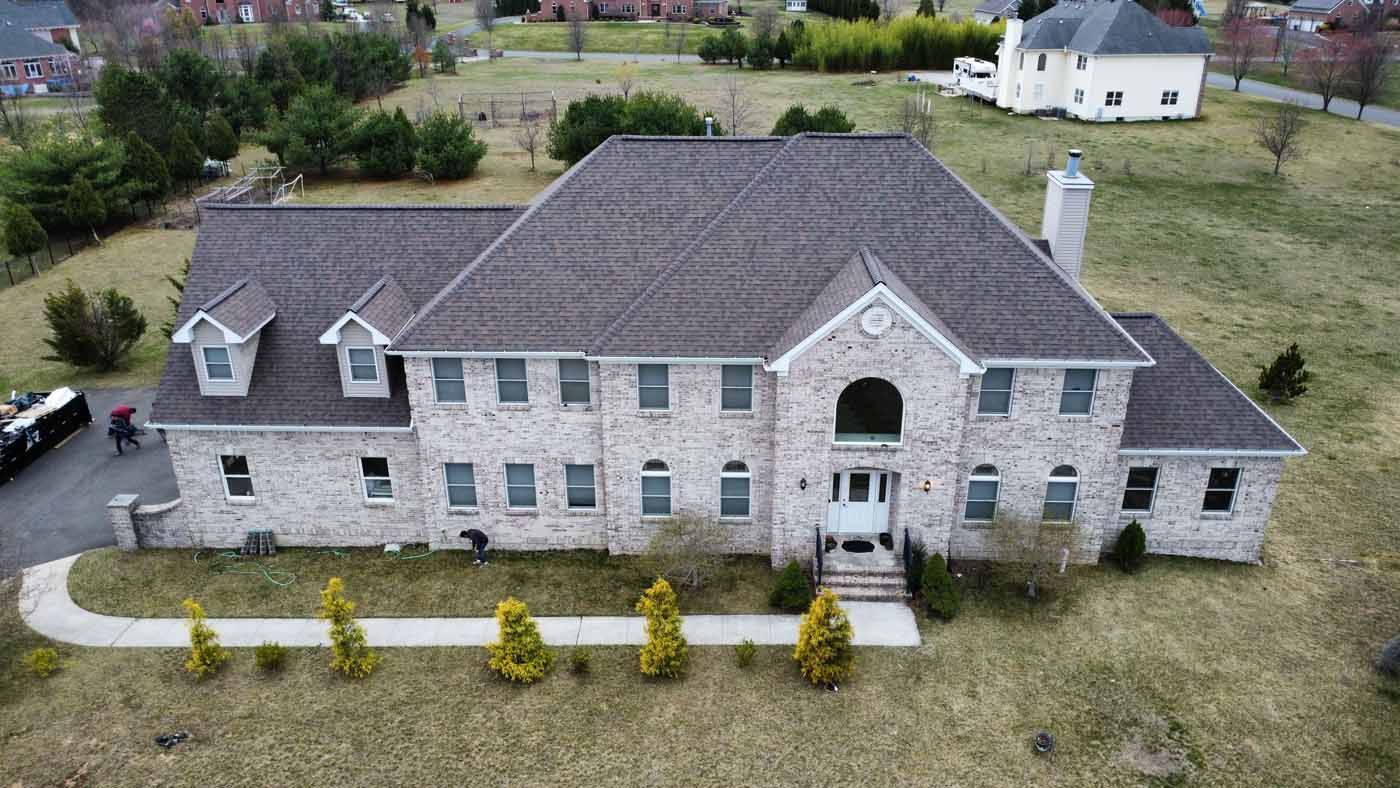 Large brick house with a gray roof and small trees in front, in a grassy yard.