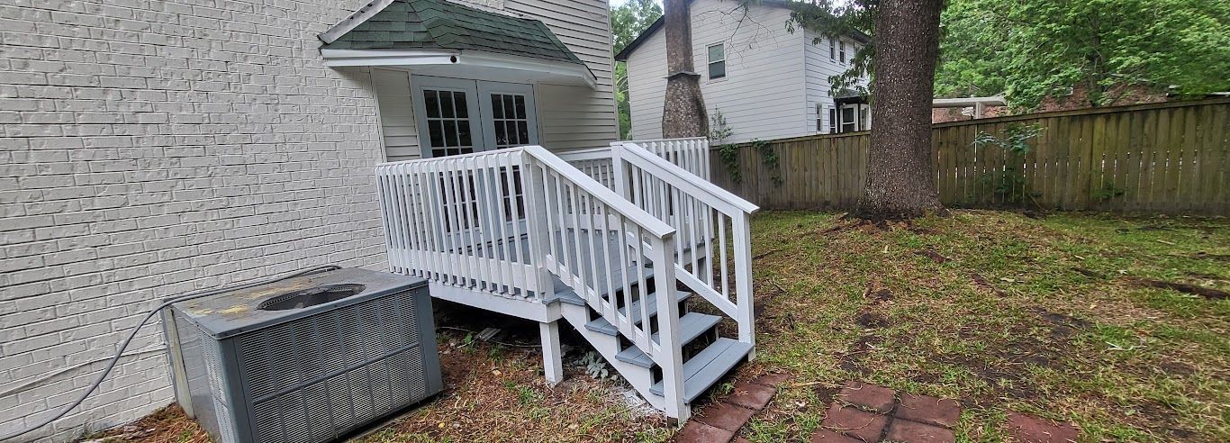A white deck with stairs leading up to it is in the backyard of a house.