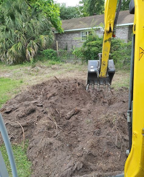 A yellow excavator is digging a hole in the dirt in a yard.