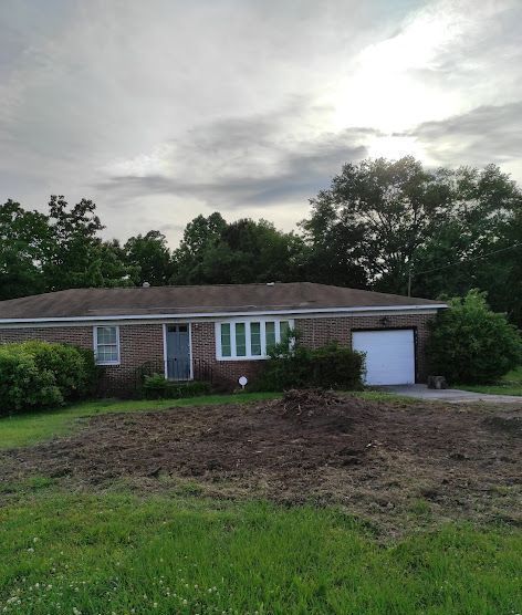 A brick house with a white garage door is surrounded by trees and grass.