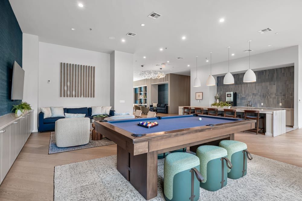 Modern open-concept living space with a pool table, kitchen island with bar stools, and a cozy sitting area featuring a large sofa, chairs, and a mounted television at 44 South in Austin, TX.