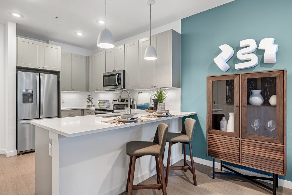Modern kitchen interior with white cabinetry, stainless steel appliances, and a central island with bar stools. The back wall is accented with a teal color. There's a wooden display cabinet with glassware on the right and a dining area partially visible in the background at 44 South in Austin, TX.