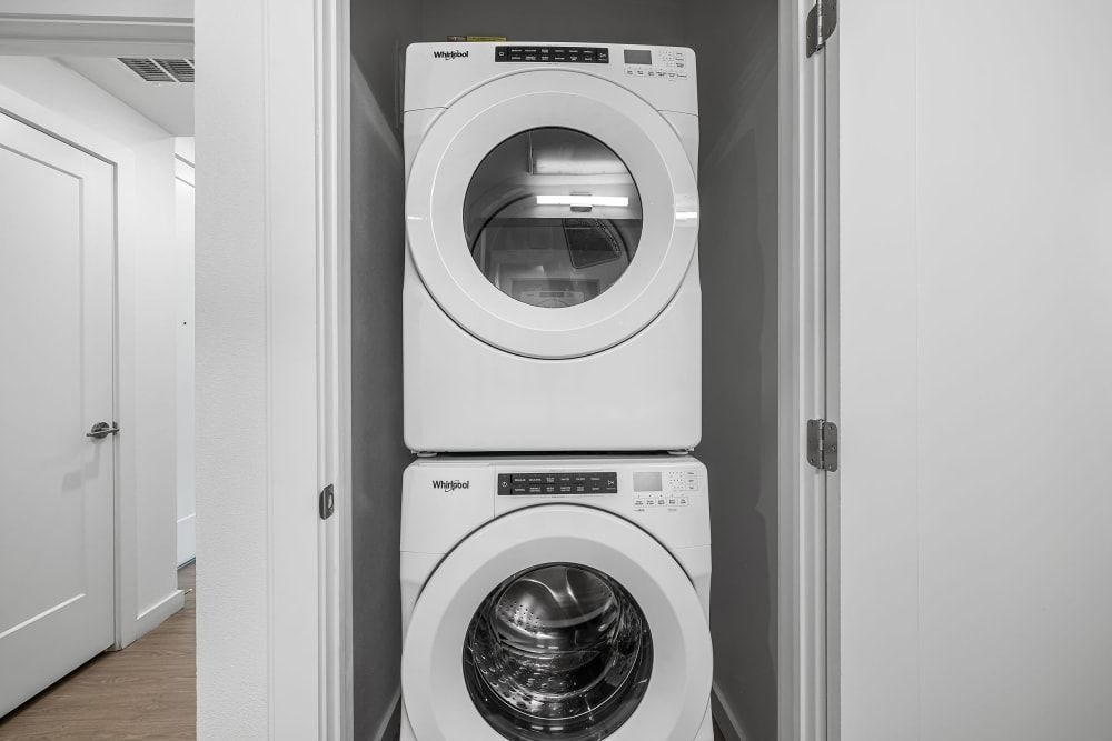 A stackable washer and dryer set by Whirlpool situated in a clean, narrow laundry closet with white walls and a hardwood floor. The washer is on the bottom and the dryer is mounted above it at 44 South in Austin, TX.