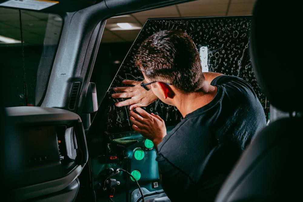 A person in a black shirt works on installing a window tint film on the inside of a vehicle’s car window.