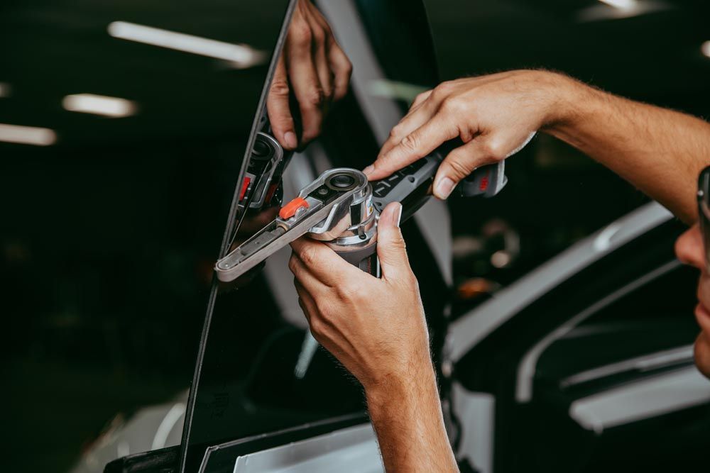 A person uses a handheld power tool to sand the edge of a glass pane in a workshop.