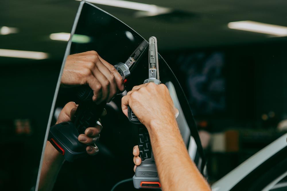 A person uses a power tool to cut or trim the adhesive seal around a vehicle's windshield in a workshop.